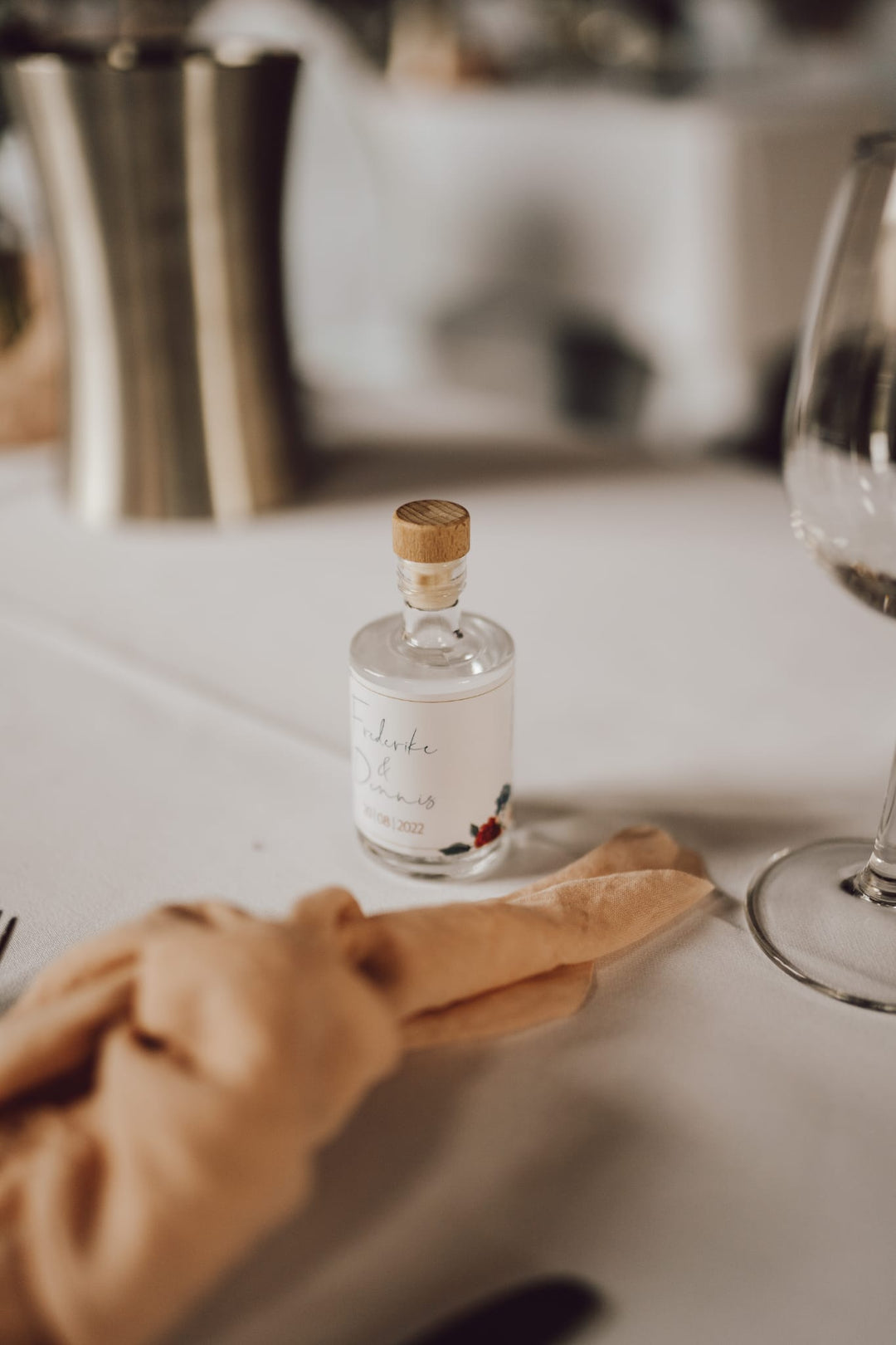 Personalisiertes Gastgeschenk zur Hochzeit: 50ml Spirituosen-Mini mit elegantem, schlichtem Etikett auf einer festlichen Tafel.