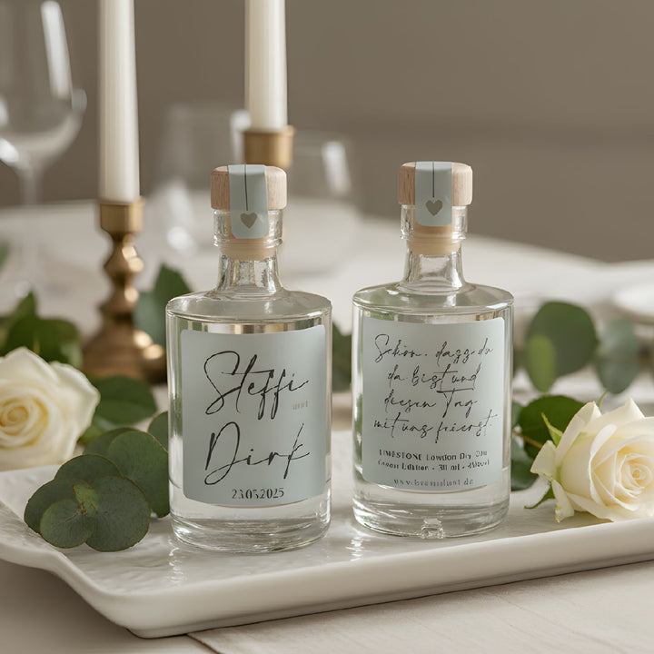 Personalisiertes Gastgeschenk zur Hochzeit: 50ml Spirituosen-Mini mit elegantem, schlichtem Etikett auf einer festlichen Tafel.