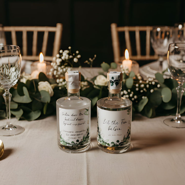 Personalisiertes Gastgeschenk zur Hochzeit: 50ml Spirituosen-Mini mit elegantem, schlichtem Etikett auf einer festlichen Tafel.