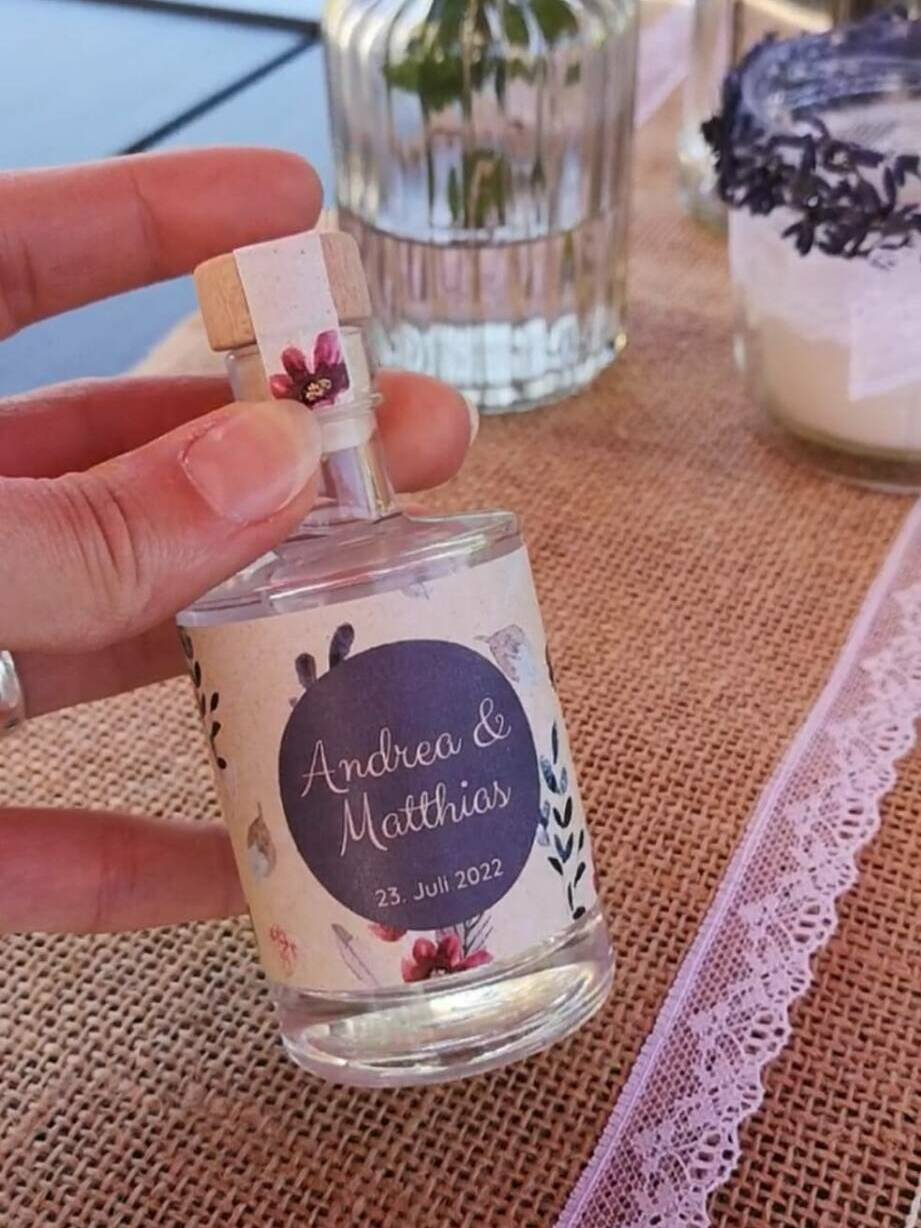 Personalisiertes Gastgeschenk zur Hochzeit: 50ml Spirituosen-Mini mit verspieltem Etikett auf einer bunter Blumen-Tafel.